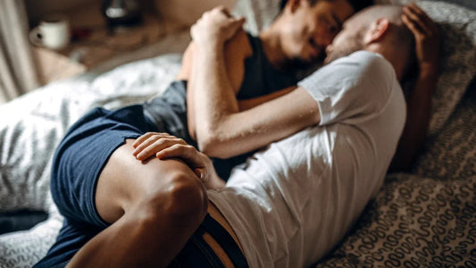 Two men lying together on a bed, relaxed and close — intimacy without the prep anxiety
