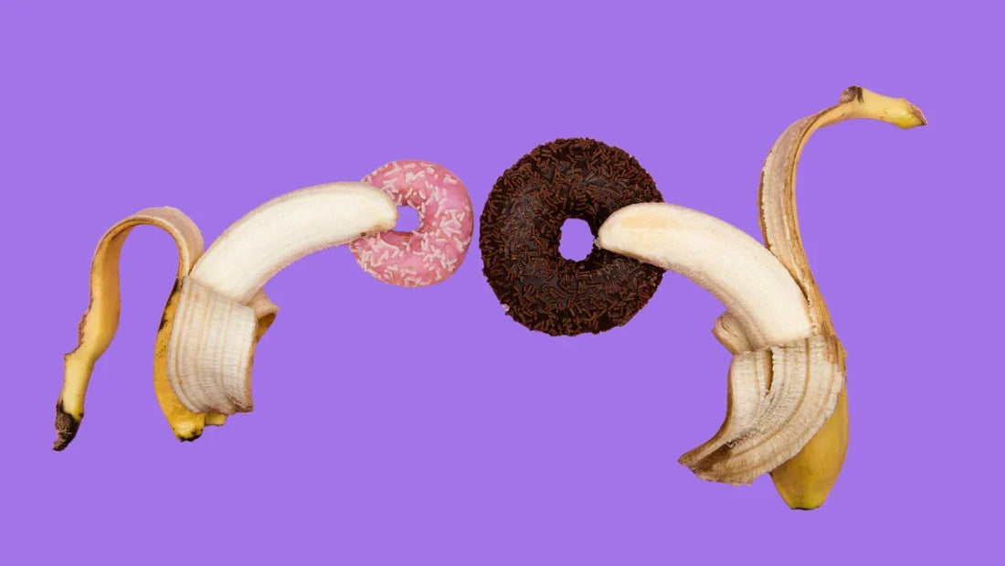 Two peeled bananas curving toward pink and chocolate donuts on a purple background, a playful visual metaphor for anal prep