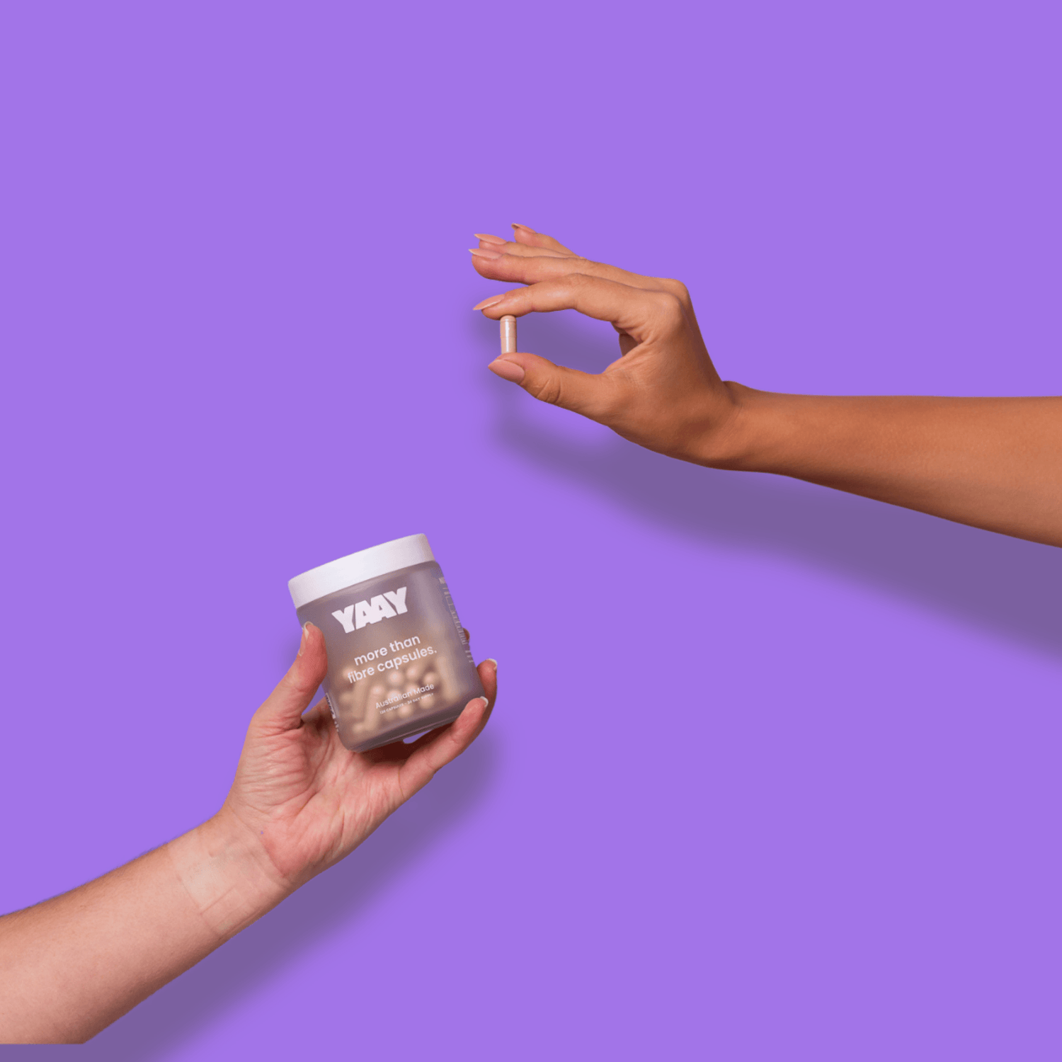 Two hands holding a 30 day supply of the YAAY More Than Fibre Capsules on a purple background